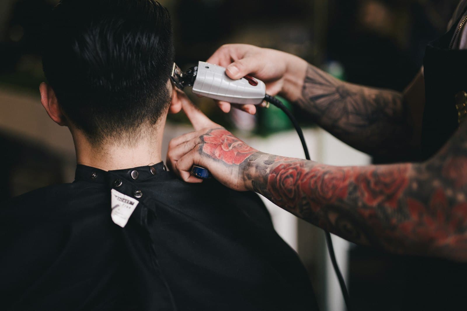 Skin fade in progress: clipper on the nape, black cape, tattooed arm